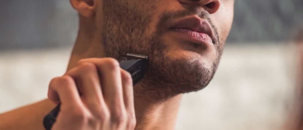 Um homem de barba rente ao rosto se barbeia com um barbeador elétrico de frente para o observador.